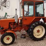 Pomarańczowy, odrestaurowany Władimirec T25 nowy, z kabiną i dużymi kołami, gotowy do pracy na polu.