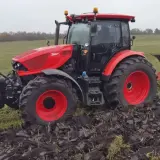 Czerwony ciągnik Zetor 6245 z pługiem orze pole w pochmurny dzień.