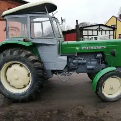 Zielony Ursus c355 z szarą kabiną, gotowy do pracy na błotnistym podwórku.