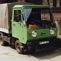 Zielony Multicar M25 z plandeką, gotowy do drogi. Obok śmietniki z napisem "Bf Harz".