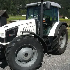 Biały traktor Hurlimann XT-130 na tle górskiego krajobrazu.