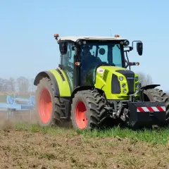 Zielony traktor Claas Arion 430 pracuje na polu, spulchniając ziemię.