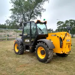 Żółty ładowarka teleskopowa JCB 531-70 stoi na trawiastym polu.