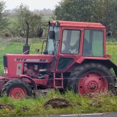 Czerwony traktor MTZ Belarus 820 pracuje na polu, za nim widać las.