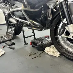 Motocykl na stojaku, narzędzia i pojemnik na zużyty olej.