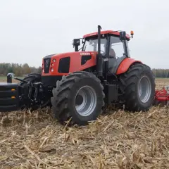 Czerwony Ursus 28014 z obciążnikiem z przodu i pługiem z tyłu pracuje na polu po żniwach.