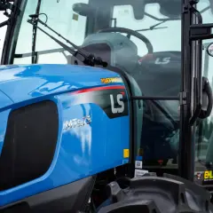 Niebieski ciągnik LS MT5.73 z napisem "POWER SHUTTLE" na błotniku. W kabinie widoczna kierownica i siedzenie.