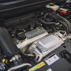 Silnik 1.6 PureTech z napisem "PEUGEOT SPORT" na metalowej osłonie. Widać turbosprężarkę i elementy układu dolotowego.