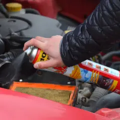 Ręka trzyma puszkę z preparatem samostart, rozpylając go do silnika samochodu.