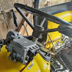 Mechanizm wspomagania kierownicy w żółtym ciągniku. Widoczna kolumna kierownicy, wał napędowy i elementy hydrauliczne.
