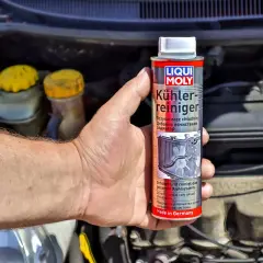 Dłoń trzyma puszkę płukanki do układu chłodzenia Liqui Moly, gotową do użycia w silniku samochodu.