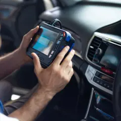 Mechanik trzymający w rękach urządzenie diagnostyczne w samochodzie.