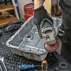 Mechanik szlifuje miskę olejową skrzyni biegów, przygotowując ją do wymiany oleju.