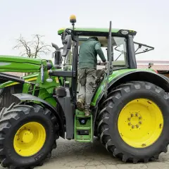 Rolnik wsiada do zielonego traktora John Deere, gotowy do pracy na gospodarstwie.