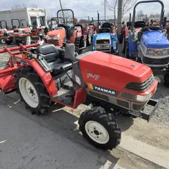 Czerwony ciągnik Yanmar F-7 z osprzętem, obok inne maszyny. Zastanawiasz się, ile oleju do skrzyni biegów?