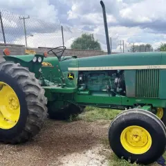 Zielony John Deere 3130 z żółtymi felgami stoi na żwirowym podwórku, gotowy do pracy.