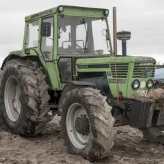 Zielony ciągnik Deutz, prawdopodobnie ciągnik bez prawa rejestracji, stoi na placu budowy.