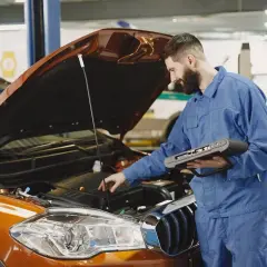 Mechanik z komputerem diagnostycznym sprawdza silnik pomarańczowego auta. Szybko dowiedz się, ile trwa wymiana oleju.