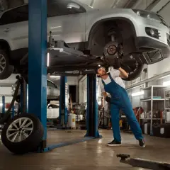Mechanik w warsztacie samochodowym naprawia podniesiony samochód.
