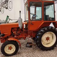 Pomarańczowy, odrestaurowany Władimirec T25 nowy, z kabiną i dużymi kołami, gotowy do pracy na polu.
