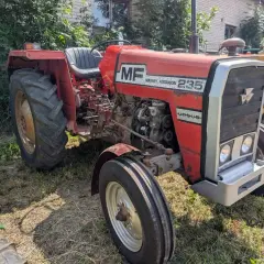 Czerwony Massey Ferguson 235 z napisem "Ursus" na masce, gotowy do pracy na polu.