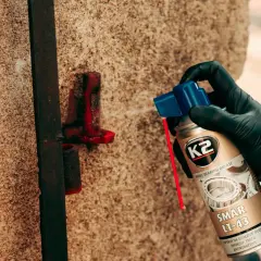 Ręka w czarnej rękawiczce aplikuje smar K2 LT-43 na zardzewiały element metalowy, chroniąc go przed korozją.