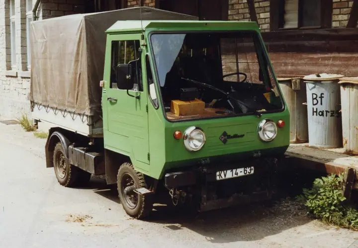 Zielony Multicar M25 z plandeką, gotowy do drogi. Obok śmietniki z napisem "Bf Harz".