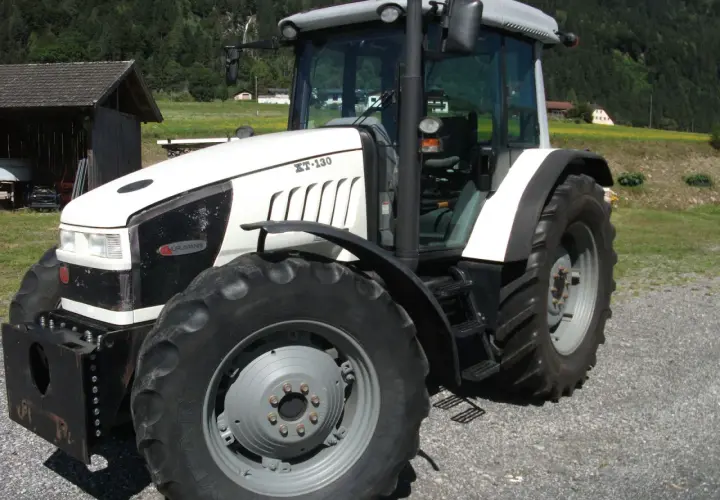 Biały traktor Hurlimann XT-130 na tle górskiego krajobrazu.