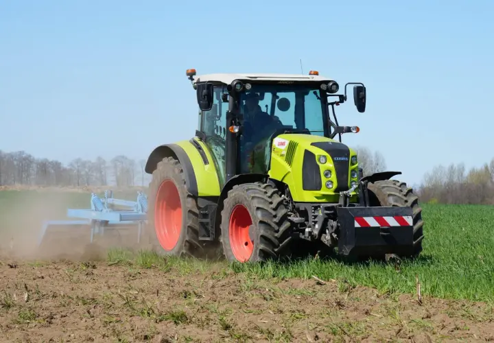 Zielony traktor Claas Arion 430 pracuje na polu, spulchniając ziemię.