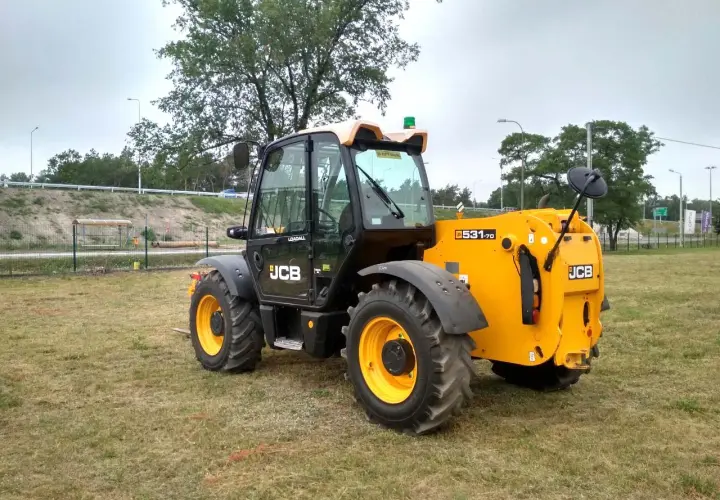 Żółty ładowarka teleskopowa JCB 531-70 stoi na trawiastym polu.