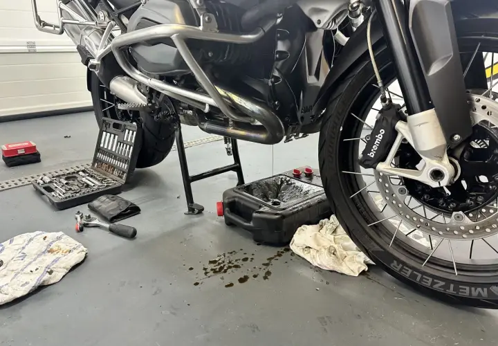 Motocykl na stojaku, narzędzia i pojemnik na zużyty olej.