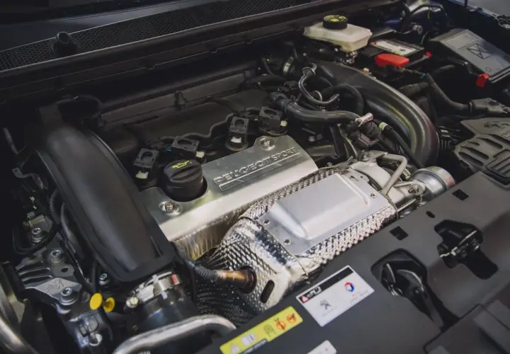 Silnik 1.6 PureTech z napisem "PEUGEOT SPORT" na metalowej osłonie. Widać turbosprężarkę i elementy układu dolotowego.