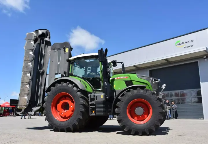 Zielony traktor Fendt 724 Vario z zamontowaną kosiarką, gotowy do pracy na polu.