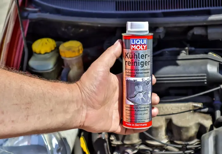 Dłoń trzyma puszkę płukanki do układu chłodzenia Liqui Moly, gotową do użycia w silniku samochodu.
