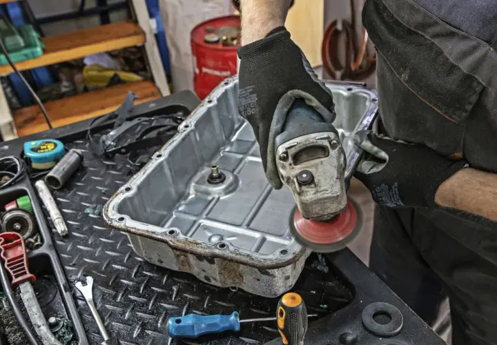 Mechanik szlifuje miskę olejową skrzyni biegów, przygotowując ją do wymiany oleju.