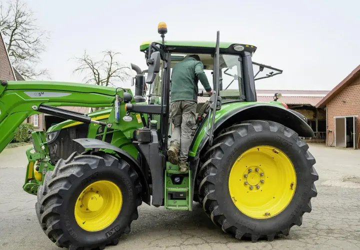 Rolnik wsiada do zielonego traktora John Deere, gotowy do pracy na gospodarstwie.