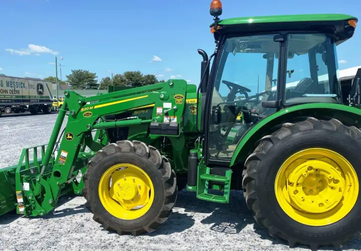 Zielony ciągnik John Deere 5075E z ładowaczem czołowym, gotowy do pracy na farmie.