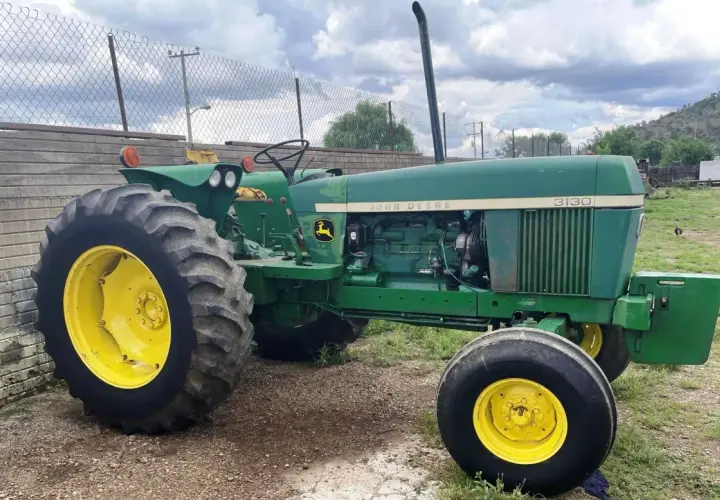 Zielony John Deere 3130 z żółtymi felgami stoi na żwirowym podwórku, gotowy do pracy.