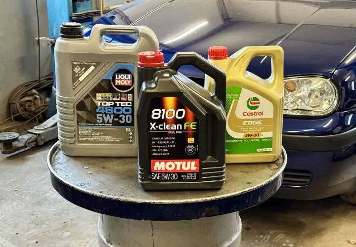 Trzy kanistry z olejem silnikowym: Liqui Moly, Motul i Castrol, na tle niebieskiego samochodu.