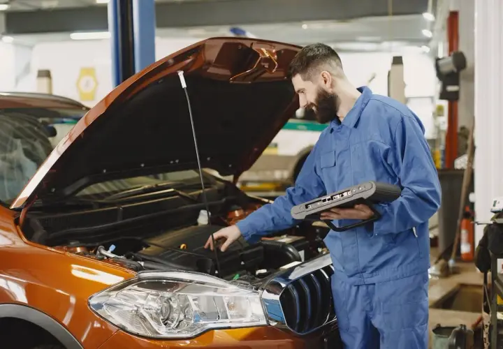 Mechanik z komputerem diagnostycznym sprawdza silnik pomarańczowego auta. Szybko dowiedz się, ile trwa wymiana oleju.