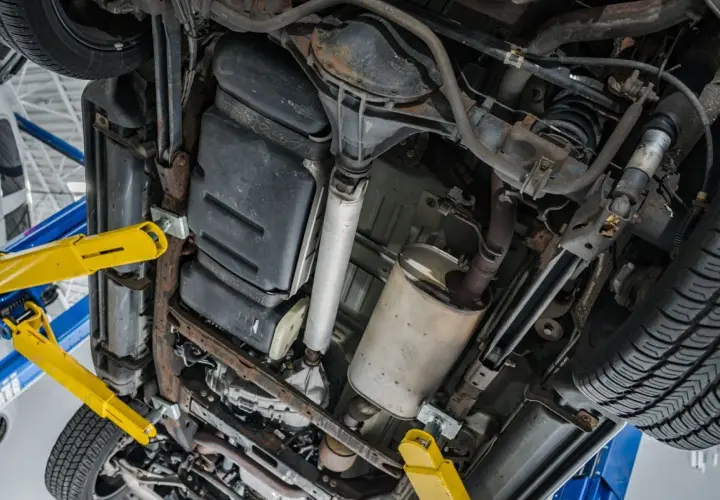 Podnośnik samochodowy podtrzymuje auto, ukazując podwozie z układem wydechowym i zbiornikiem paliwa. Czas na wypalanie DPF.
