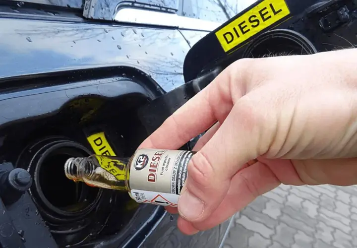 Dłoń wlewa dodatek do benzyny do baku samochodu z napisem DIESEL.