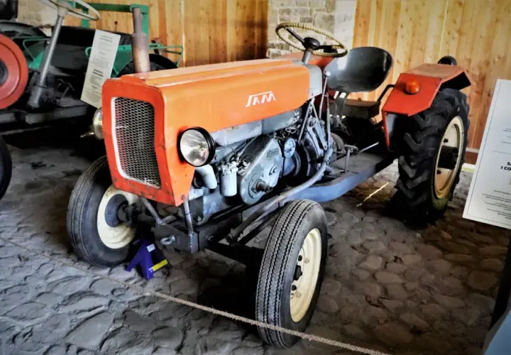 Pomarańczowy traktor SAM, znany jako esiok, z charakterystycznym grillem i silnikiem.