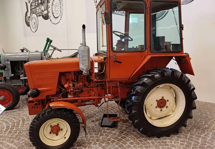 Pomarańczowy, odrestaurowany Władimirec T25 nowy, z kabiną i dużymi kołami, gotowy do pracy na polu.