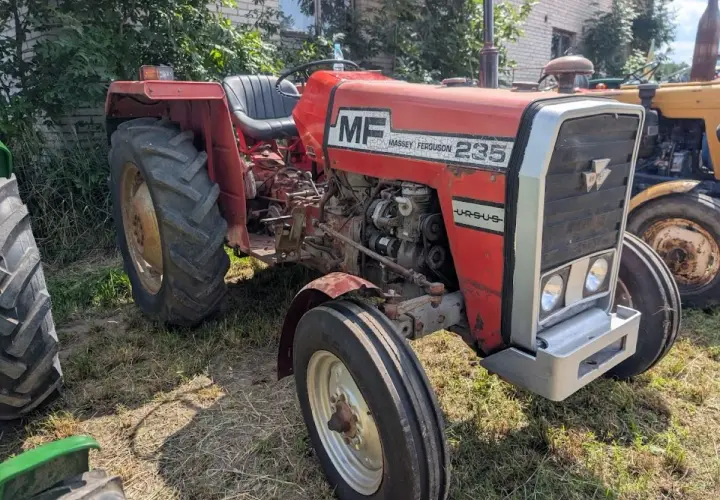 Czerwony Massey Ferguson 235 z napisem "Ursus" na masce, gotowy do pracy na polu.