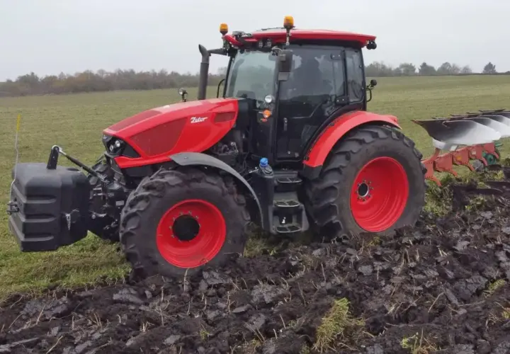 Czerwony ciągnik Zetor 6245 z pługiem orze pole w pochmurny dzień.