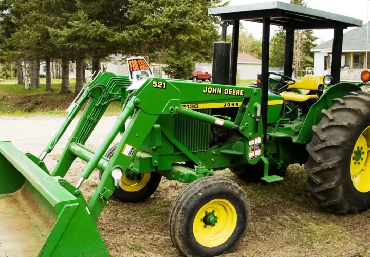 Zielony traktor John Deere 2130 z ładowaczem czołowym stoi na podwórku, gotowy do pracy.