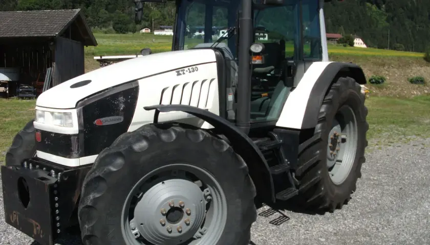 Biały traktor Hurlimann XT-130 na tle górskiego krajobrazu.