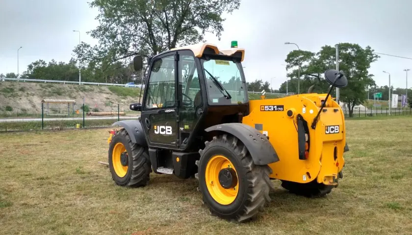 Żółty ładowarka teleskopowa JCB 531-70 stoi na trawiastym polu.