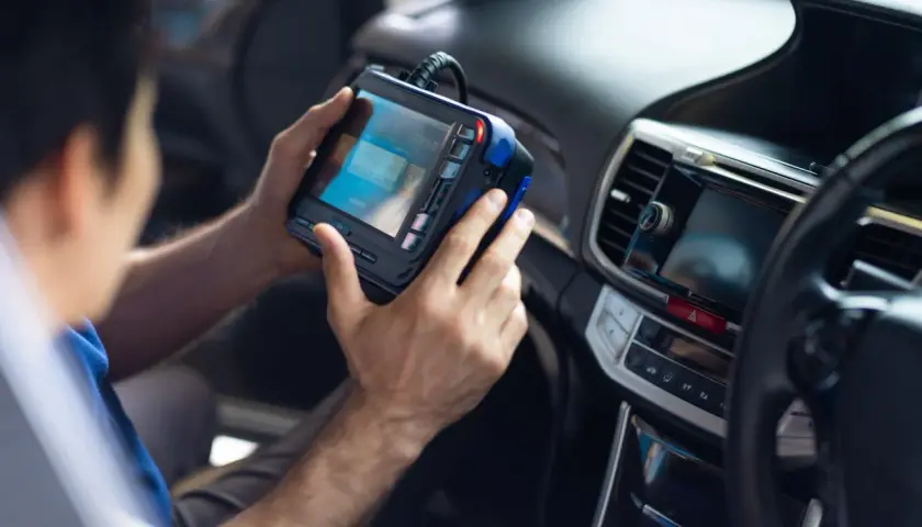 Mechanik trzymający w rękach urządzenie diagnostyczne w samochodzie.